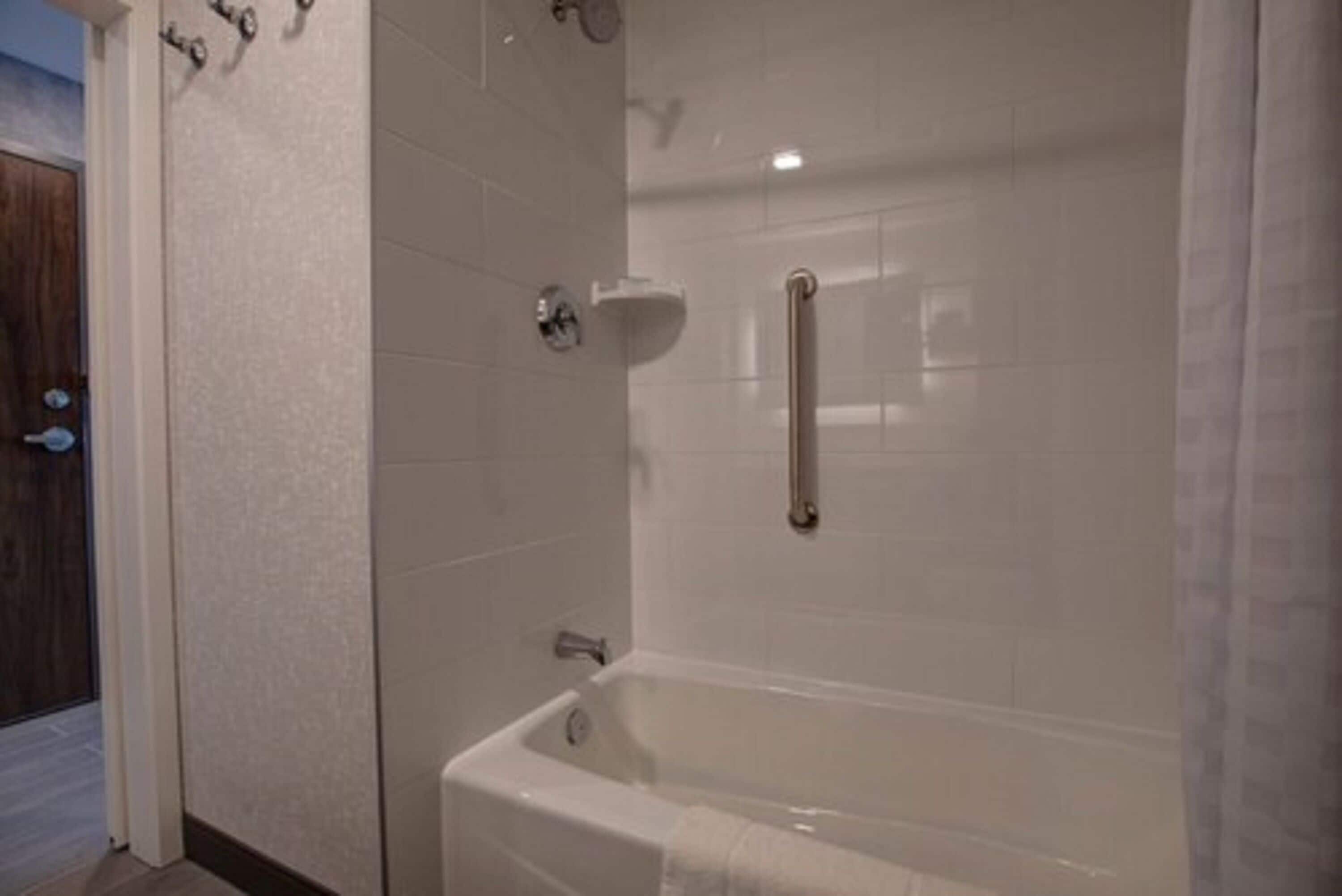 Un baño con bañera, zona de ducha y barra de apoyo.