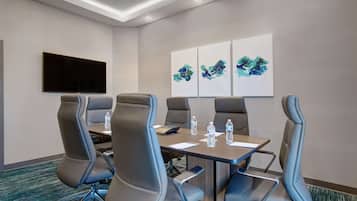 A conference room with a large table, six chairs, a flat-screen TV, and abstract wall art.