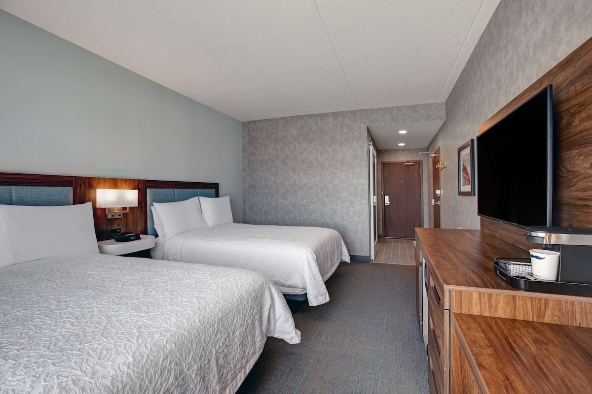 A hotel room with two beds, a TV, a desk, and a bathroom visible through an open door.