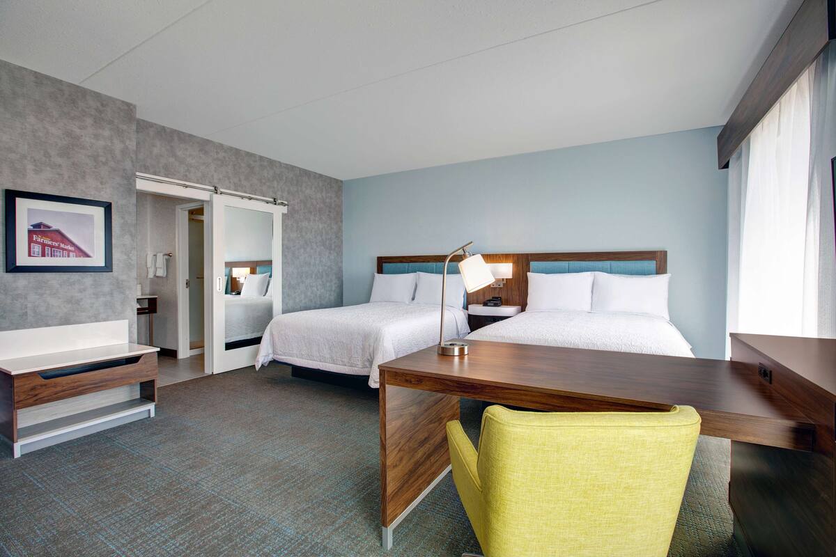 A hotel room with two beds, a desk, a chair, and a bedside table.