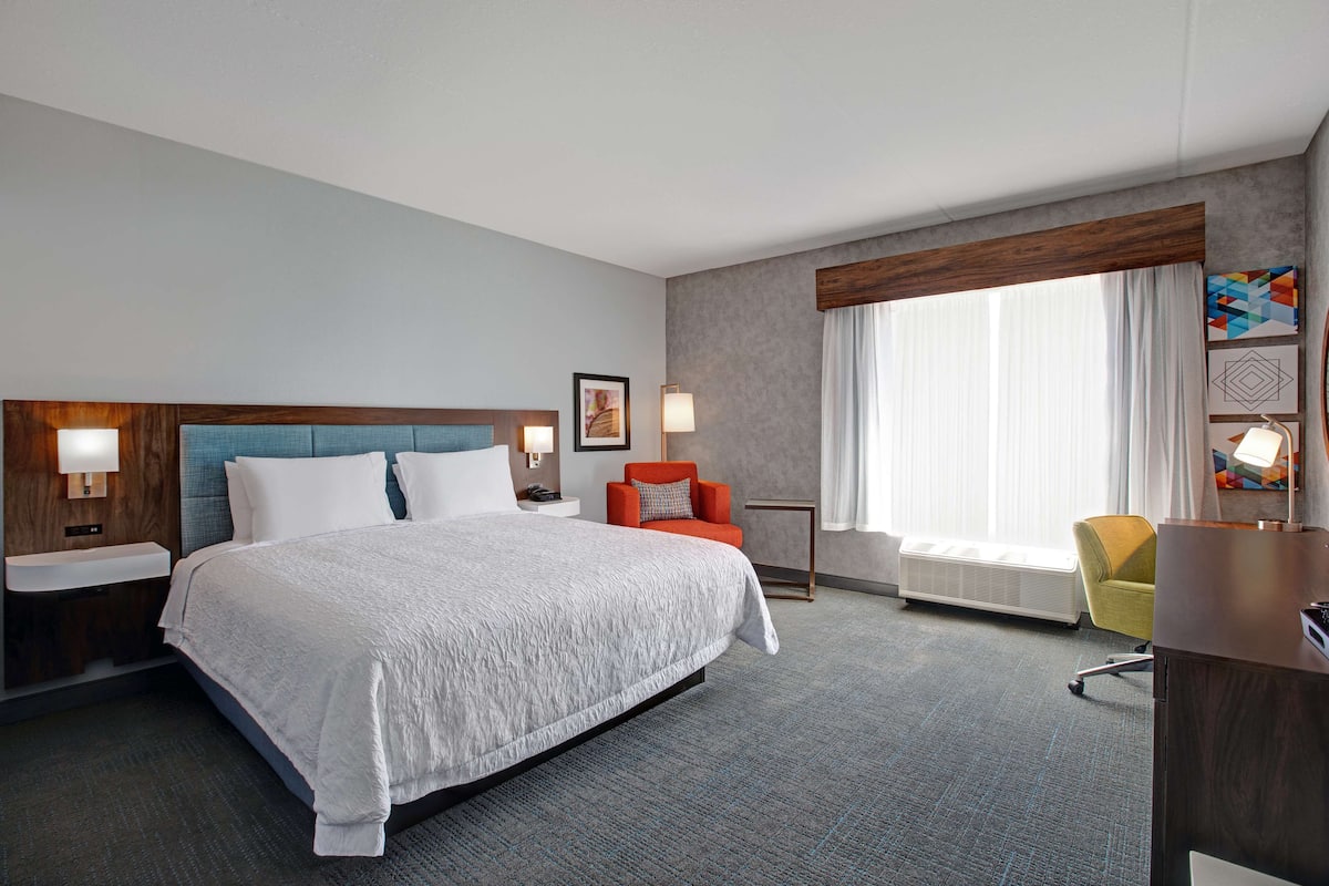 A hotel room with a large bed, a desk, a chair, and a window with curtains.