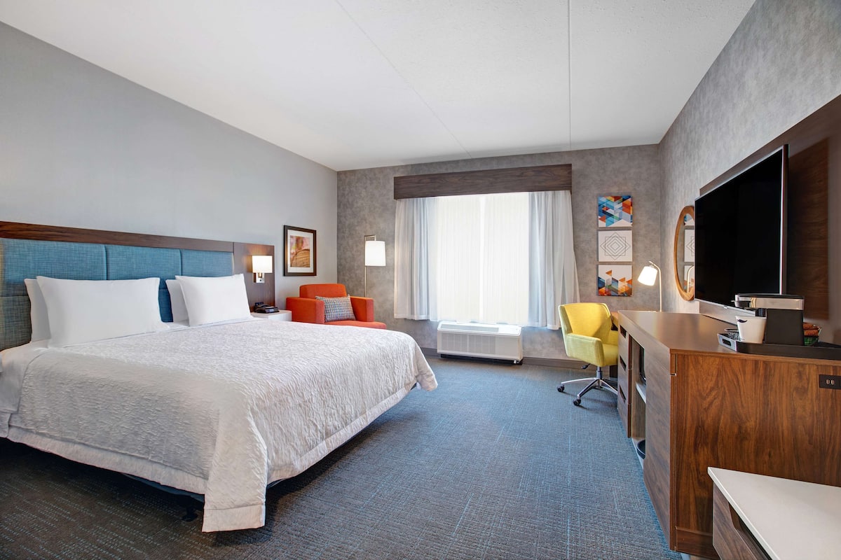 A hotel room with a large bed, a desk, a chair, a TV, and a window with curtains.