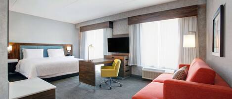 A hotel room with a bed, desk, chair, TV, and a red sofa.