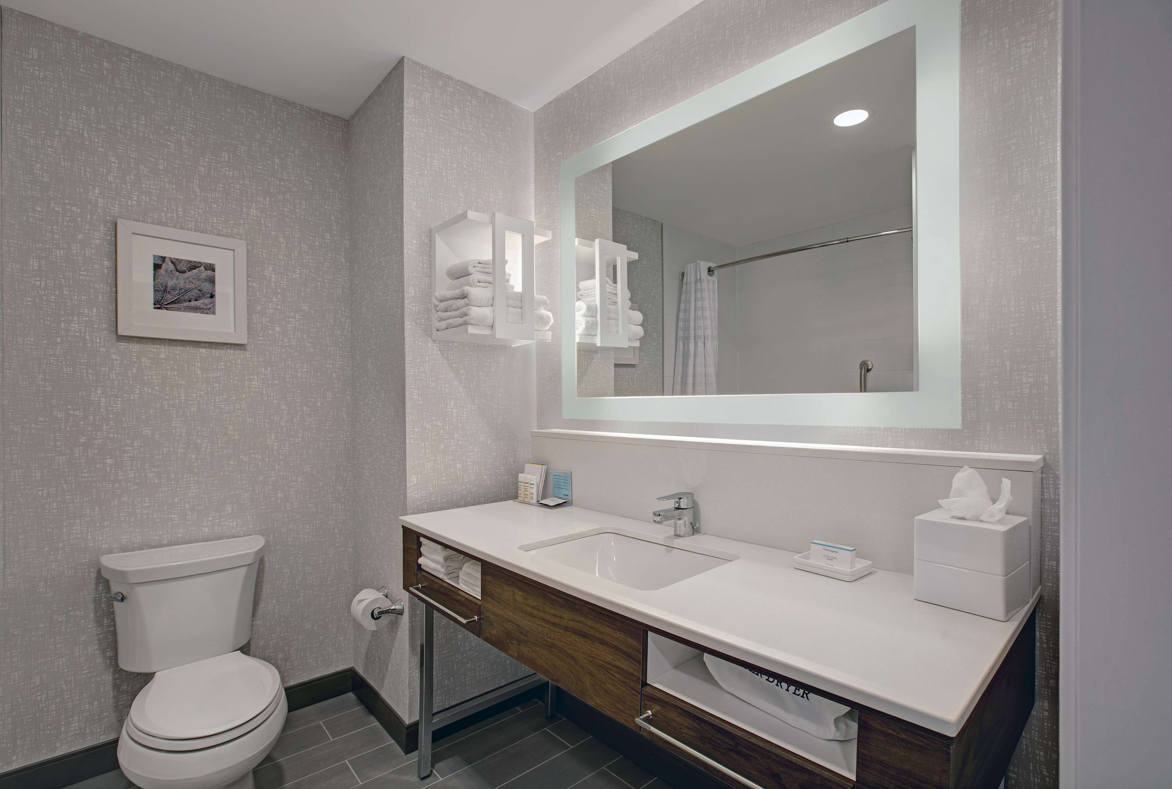 A modern bathroom with a white toilet, a large mirror, a sink with a vanity, and a framed picture on the wall.
