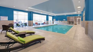 An indoor swimming pool with lounge chairs, a poolside table, and a view of the outside. - Hampton Inn & Suites by Hilton Waterloo St. Jacobs (Township of Woolwich)