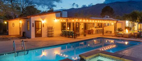 A poolside area with a hot tub, outdoor seating, and a building with string lights.