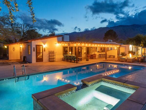 A poolside area with a hot tub, outdoor seating, and a building with string lights.