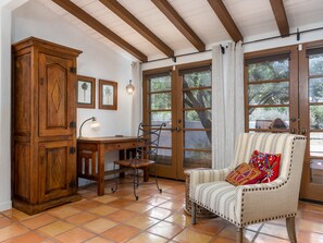 A room with a wooden cabinet, a desk, a chair, and large windows with curtains.