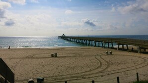 Une plage avec une jetée qui s’avance dans l’océan, une plage de sable et un ciel dégagé.