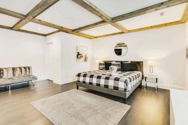 A bedroom with a bed, a sofa, a round mirror, and a bedside table.