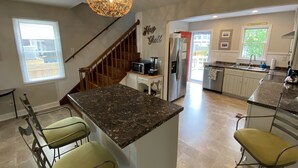 A modern kitchen with a central island, bar stools, a stainless steel refrigerator, and a decorative ceiling light.