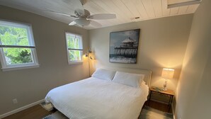 A bedroom with a bed, two bedside lamps, a ceiling fan, and a painting on the wall.
