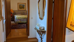 A hallway with a chandelier, a mirror, a bedside table with a candle, and a bed with a floral bedspread.