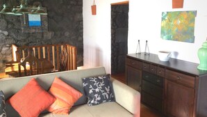 A living room with a stone wall, a wooden chair, a sofa with patterned cushions, a cabinet, and a painting on the wall.