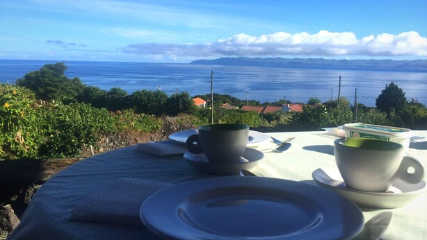 A table with cups and plates set for a meal, overlooking a scenic view of the sea and distant mountains.