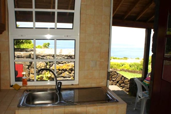 Cozinha com pia, janela com vista para o mar e parede de pedra externa.