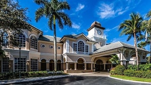 A large, two-story building with a central clock tower, arched windows, and a covered entrance area. - PARADISE FOUND! NOW BOOKING FOR 2026! (Naples)