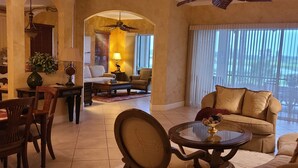 A spacious living area with a sofa, armchairs, a coffee table, and a dining table with chairs. There is a view of the outdoors through large windows. - PARADISE FOUND! NOW BOOKING FOR 2026! (Naples)