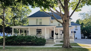 A two-story house with a porch, a covered entryway, and a large tree in front. - CENTRAL A/C!!! Huge Downtown Historic CVX Home! Walk to town & beach! (Charlevoix)