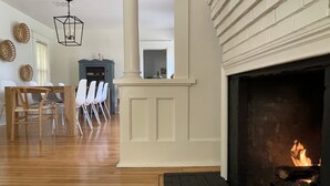 A living room with a fireplace, wooden flooring, a dining area with chairs, and a ceiling light fixture. - CENTRAL A/C!!! Huge Downtown Historic CVX Home! Walk to town & beach! (Charlevoix)