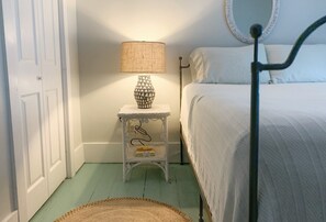 A bedroom with a bed, a bedside table with a lamp, a mirror, and a door.