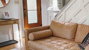 A room with a beige leather sofa, a white armchair, a wooden side table, and a mirror. - CENTRAL A/C!!! Huge Downtown Historic CVX Home! Walk to town & beach! (Charlevoix)