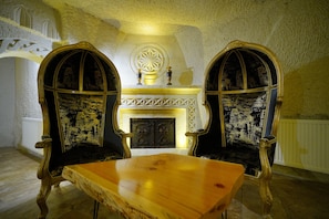 Una habitación con dos sillones ornamentados, una mesa de madera, una chimenea decorativa y un muro de piedra.