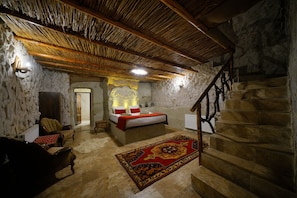 A stone-walled bedroom with a bed, a wooden staircase, and a red carpet. - Nar Cave House (Nevşehir)