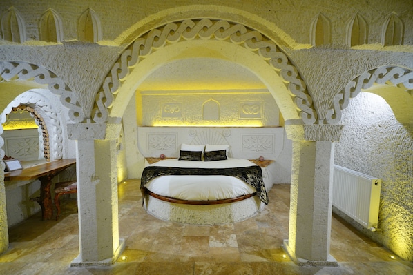 A circular bed with a white and black bedspread, surrounded by ornate stone arches and a stone floor. - Nar Cave House (Nevşehir)