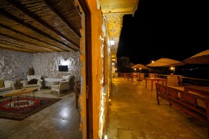 Un área de descanso al aire libre con paredes de piedra, muebles de madera y sombrillas de paja.