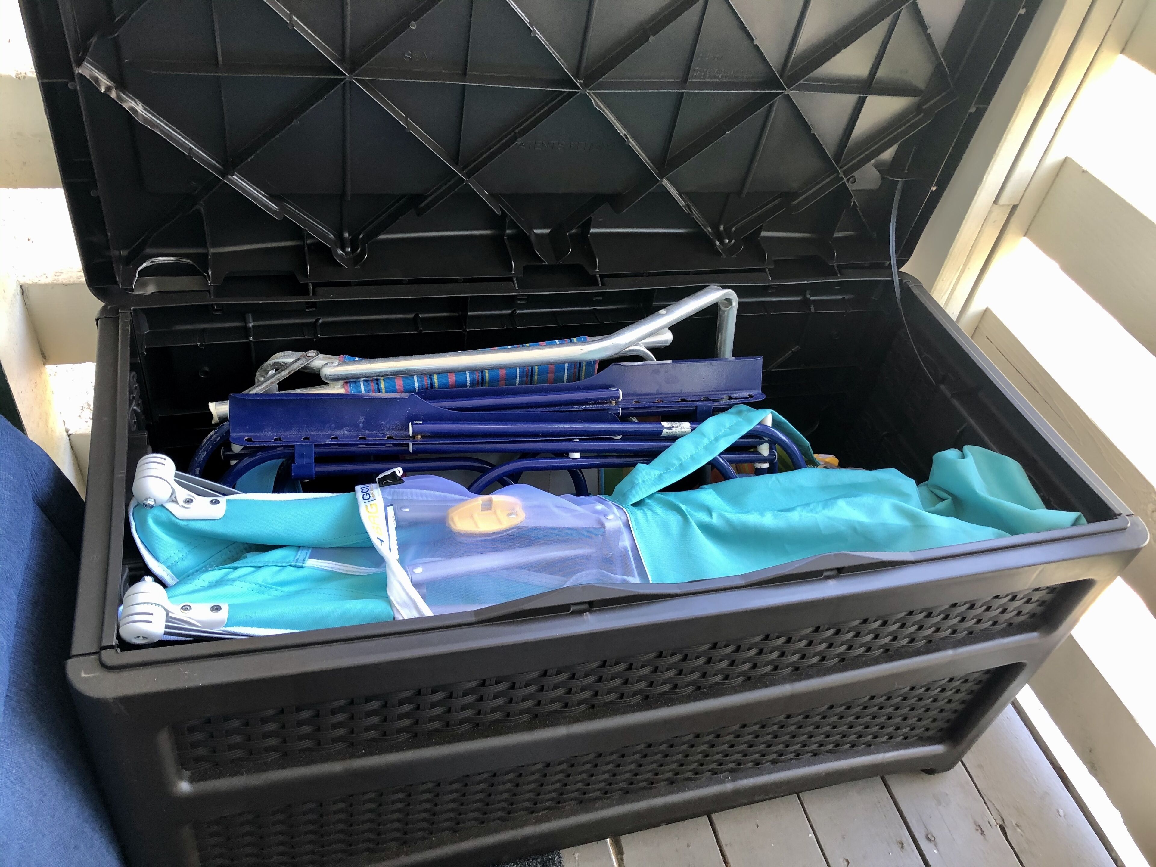 A black storage bin with a mesh bottom, containing various items including a blue bag and a blue item with a white strap.