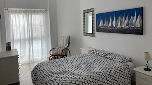 A bedroom with a bed, a chair, a dresser, a mirror, and a painting of sailboats. - Nice and cozy apartment, private parking and sea views in Cabo de Palos. (Cabo de Palos)