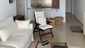 A modern living room with a sofa, a coffee table, and a chair. A kitchen is visible in the background with wooden cabinets and a window. - Nice and cozy apartment, private parking and sea views in Cabo de Palos. (Cabo de Palos)