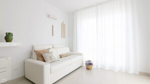 A minimalist white living room with a white sofa, a green vase on a shelf, and a basket with a book.