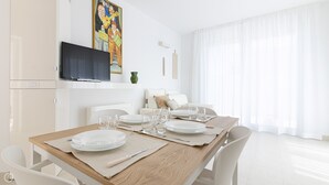 A modern dining area with a wooden table set for four, white chairs, and a television mounted on a cabinet.