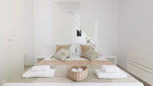 A modern bedroom with a large bed, two bedside tables, a mirror, and a wall-mounted light fixture.