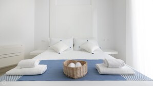 Una cama bien hecha con sábanas blancas, una colcha azul y una cesta de toallas.