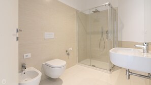Et moderne badeværelse med bruseniche i glas, et bidet, et toilet og en stor vask.