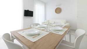 A dining area with a wooden table set for four, white chairs, and a white sofa in the background. - Rivazzurra Homes - 52 (Termoli)