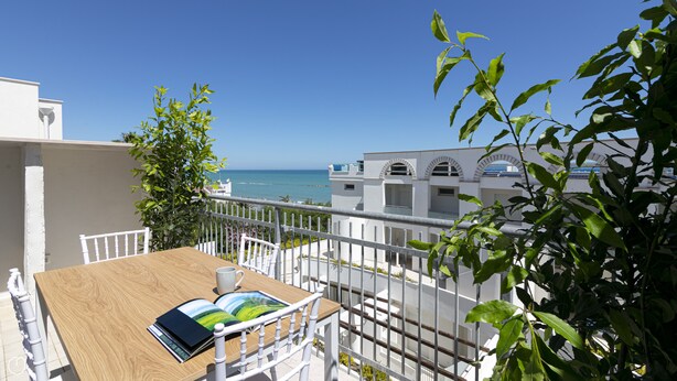 A balcony with a wooden table, white chairs, and a view of the sea. - Rivazzurra Homes - 52 (Termoli)