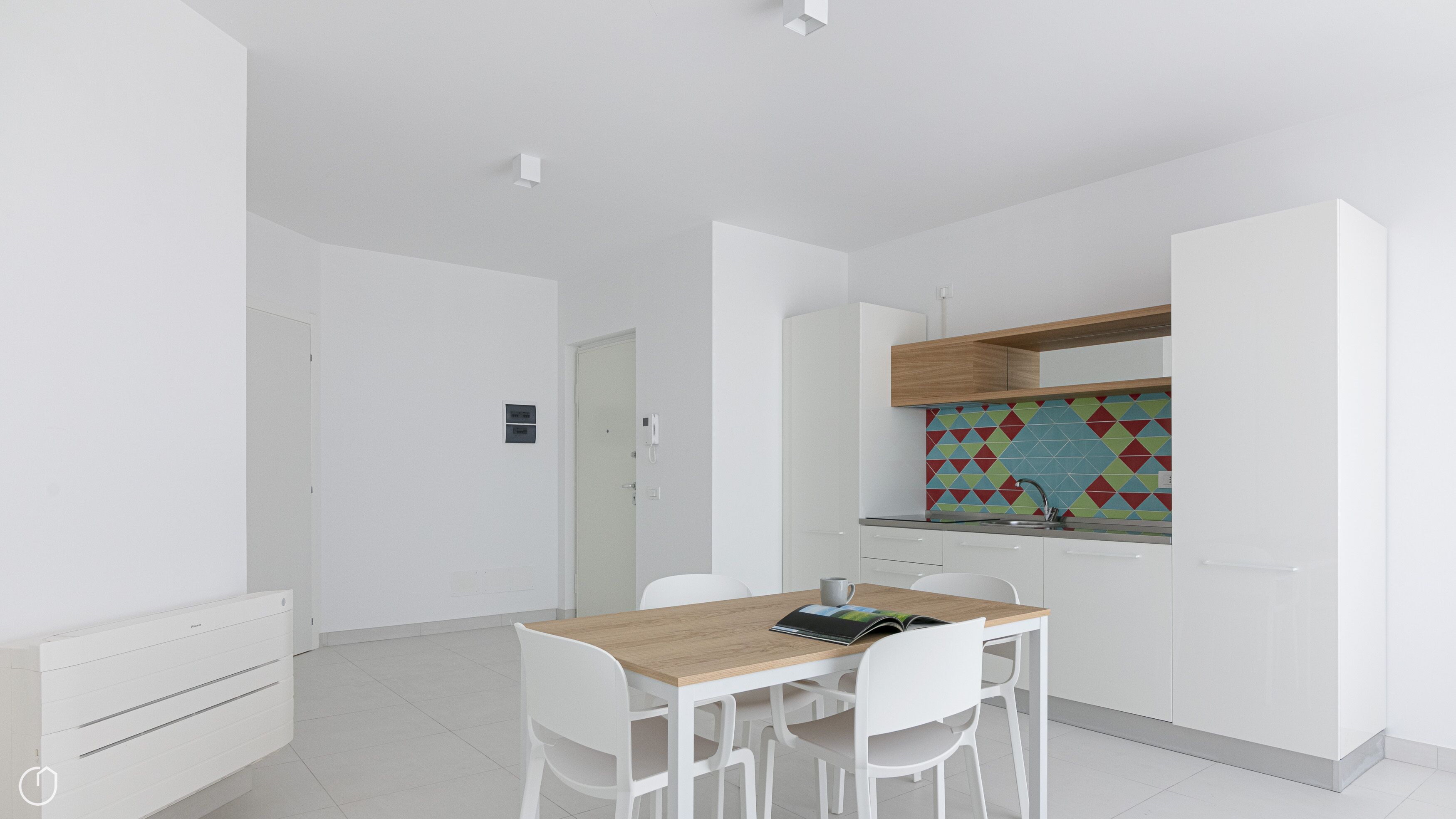 Une cuisine moderne avec des meubles blancs, un plan de travail en bois et un revêtement mural coloré. On y trouve également un coin repas avec une table et des chaises blanches.