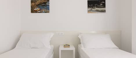 Une chambre d’hôtel avec deux lits simples, une petite table de chevet sur laquelle se trouve un livre, et deux tableaux encadrés accrochés au mur.