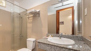 A modern bathroom with a glass shower enclosure, a white toilet, a granite countertop with a sink, and a large mirror. - White Lion Hotel Nha Trang (Nha Trang)