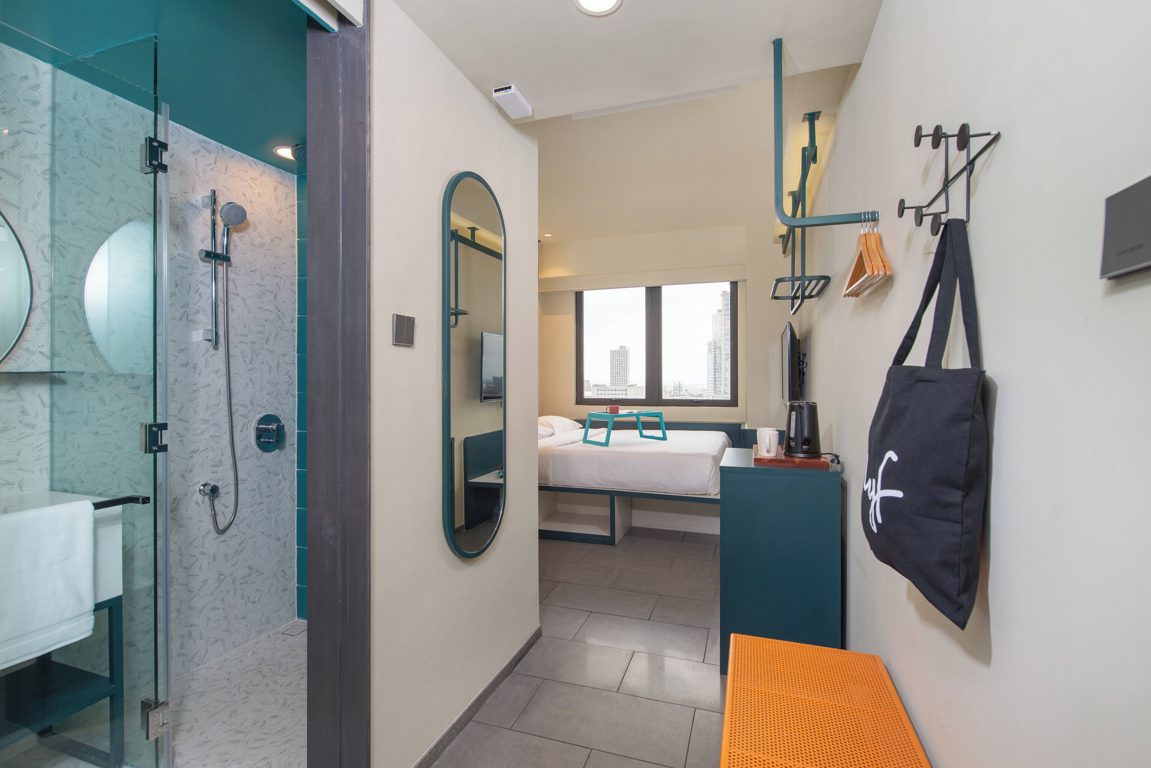 A modern hotel room with a shower, a bed, a desk, and a view of the city.