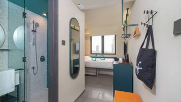 A modern hotel room with a shower, a bed, a desk, and a view of the city.