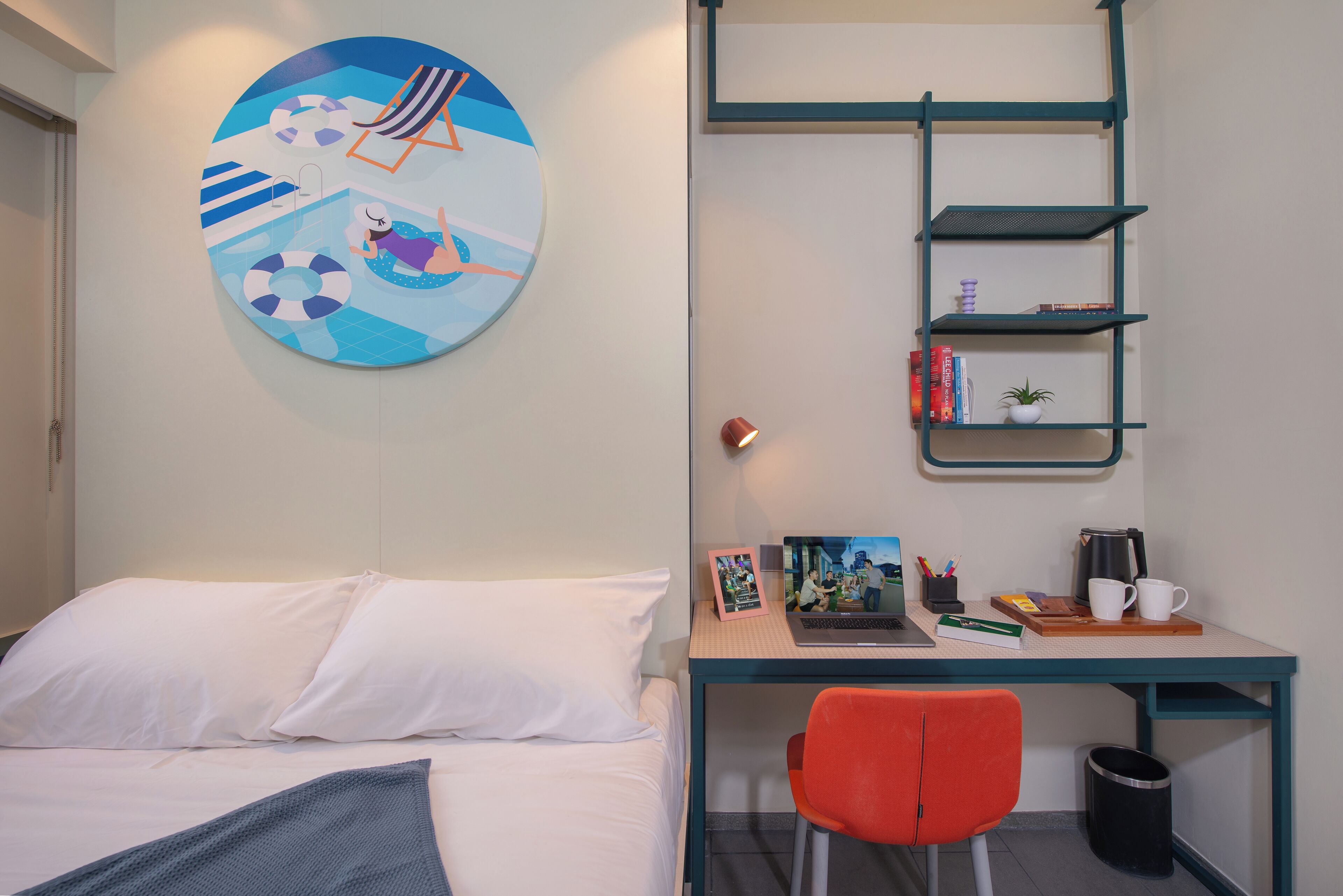 A bedroom with a bed, a desk with a chair, a bookshelf, and a wall with a circular artwork.
