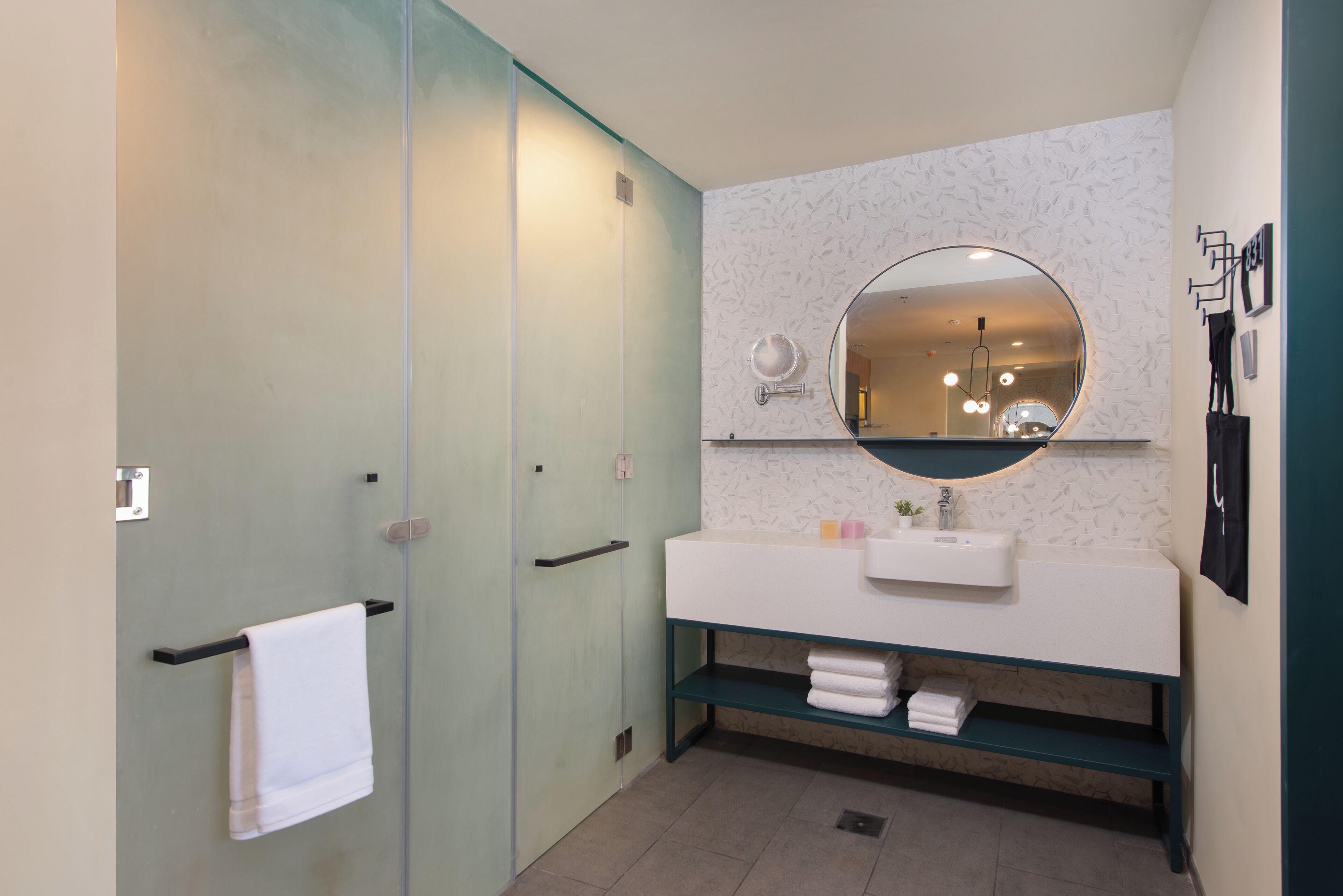 A modern bathroom with a glass shower enclosure, a white sink with a round mirror, and a towel rack.