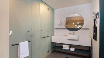 A modern bathroom with a glass shower enclosure, a white sink with a round mirror, and a towel rack.