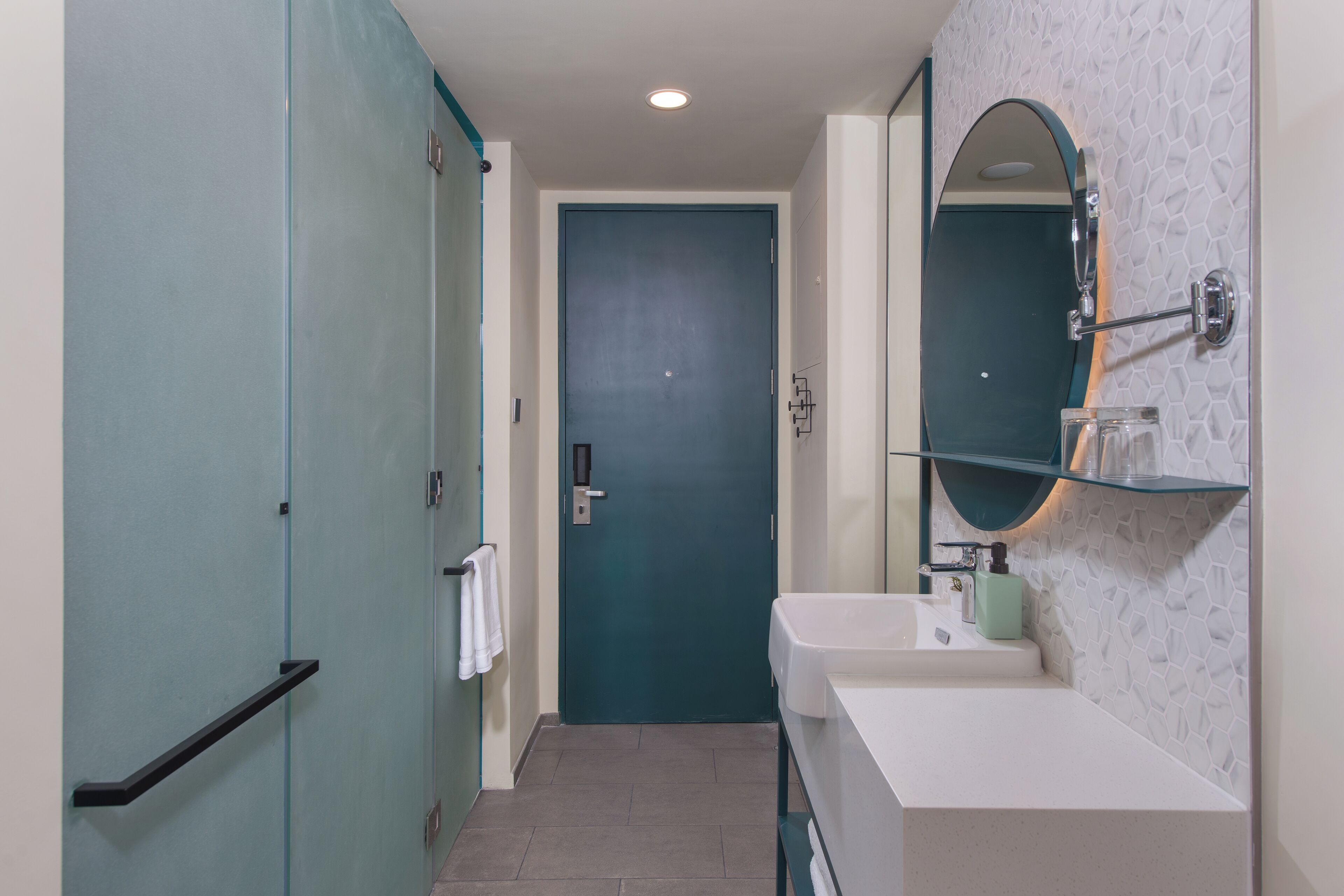 A bathroom with a teal door, white sink, and a mirror with a teal frame.