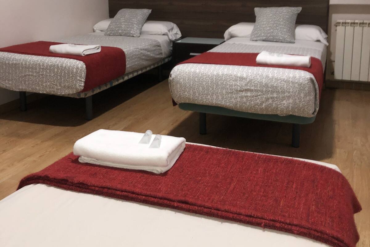 A hotel room with two single beds, each with a red and white blanket, and a red blanket on the floor.